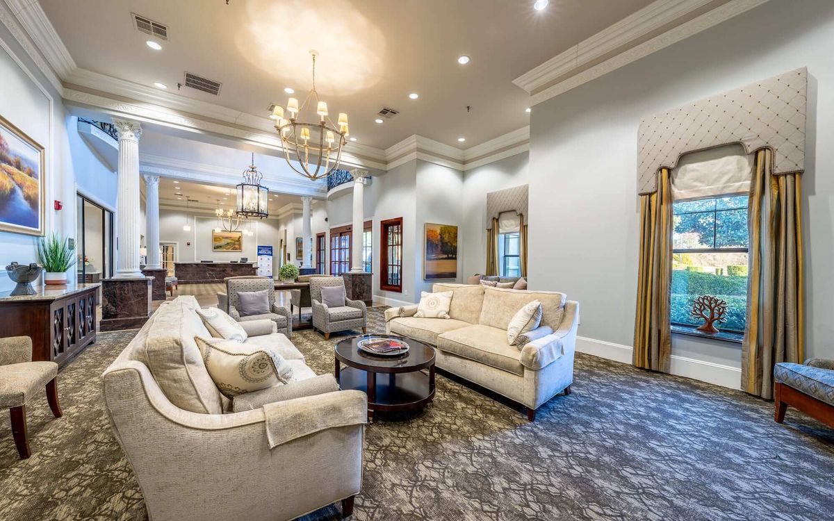 A spacious and elegant living room with plush sofas, a central coffee table, and a grand chandelier.