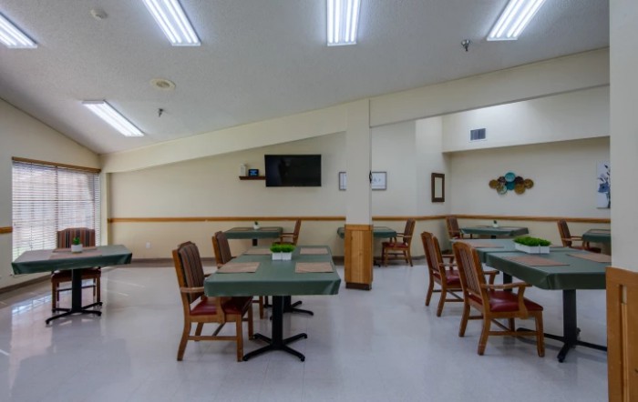 A well-lit dining area with several tables and chairs, featuring a wall-mounted television.