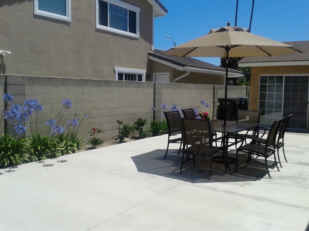 A sunny backyard patio with a table, chairs, and an umbrella.