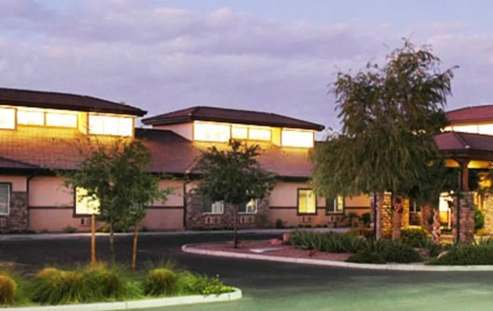 A building illuminated by soft evening lights with surrounding trees and a cloudy sky.