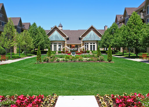 A stunning view of a spacious house surrounded by a beautifully maintained garden and lush green lawn under a clear blue sky.