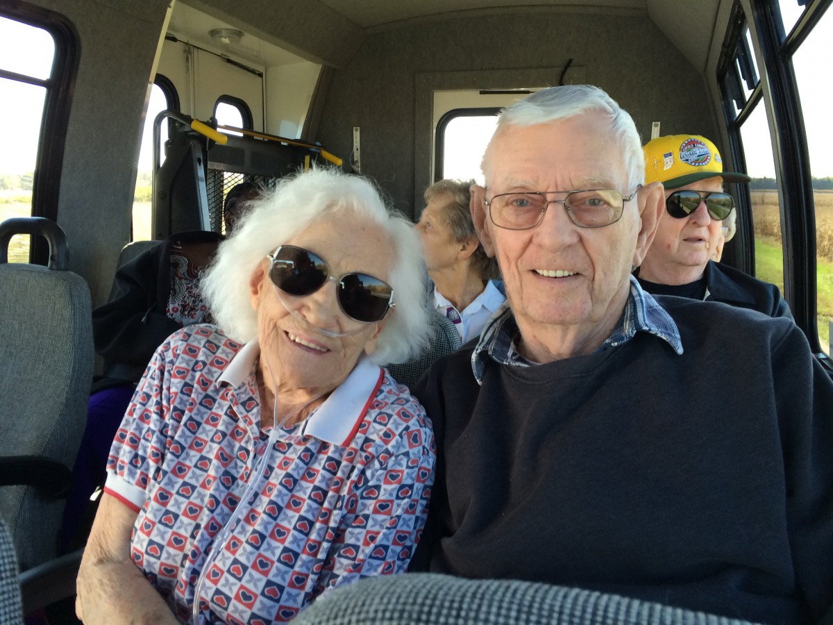 An elderly couple wearing sunglasses and smiling while sitting inside a vehicle.