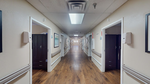 A well-lit corridor in a hospital, featuring polished wooden floors and doors to patient rooms.