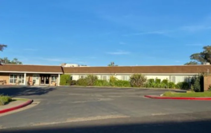A wide, single-story building with a parking lot in the foreground and clear blue sky above.