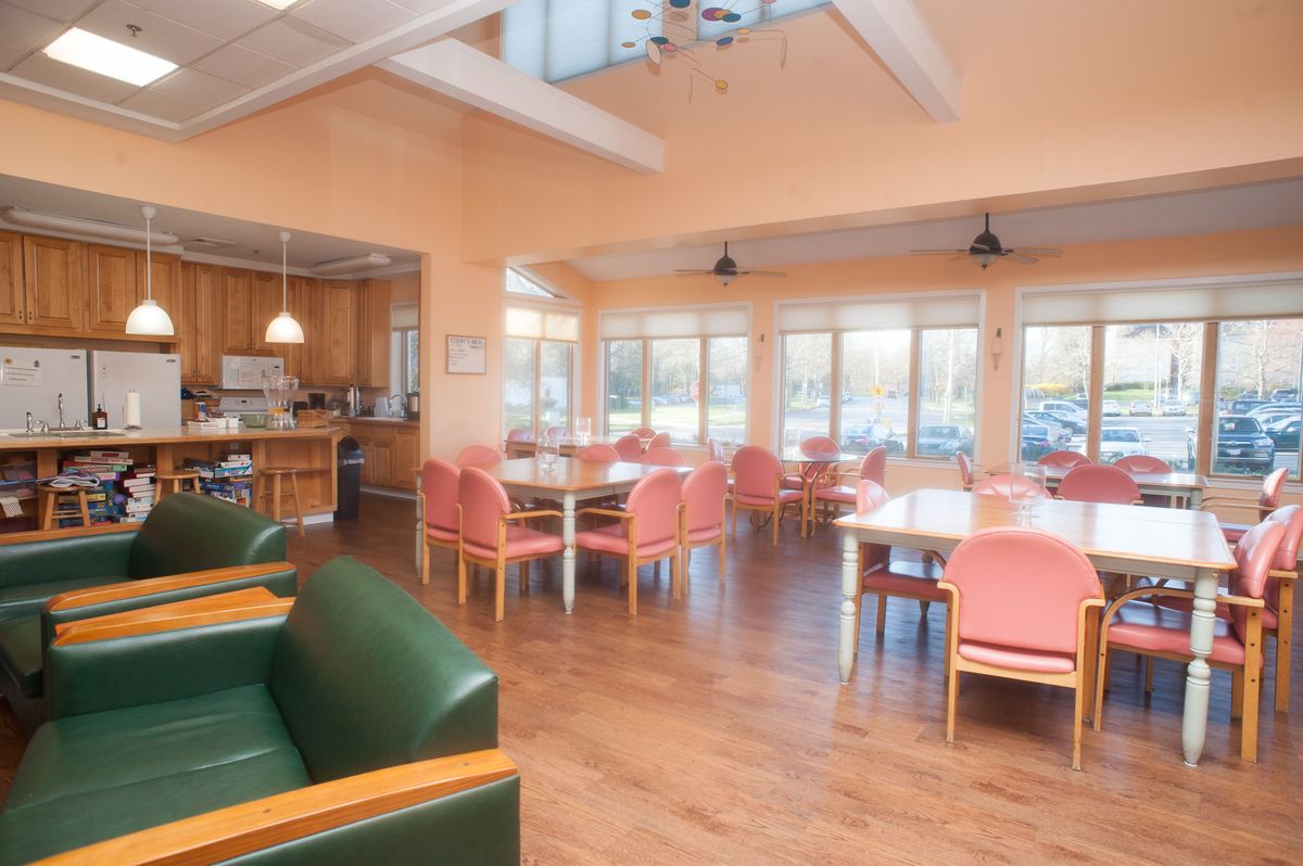 A bright and spacious dining area with a kitchen, featuring tables and chairs near large windows.