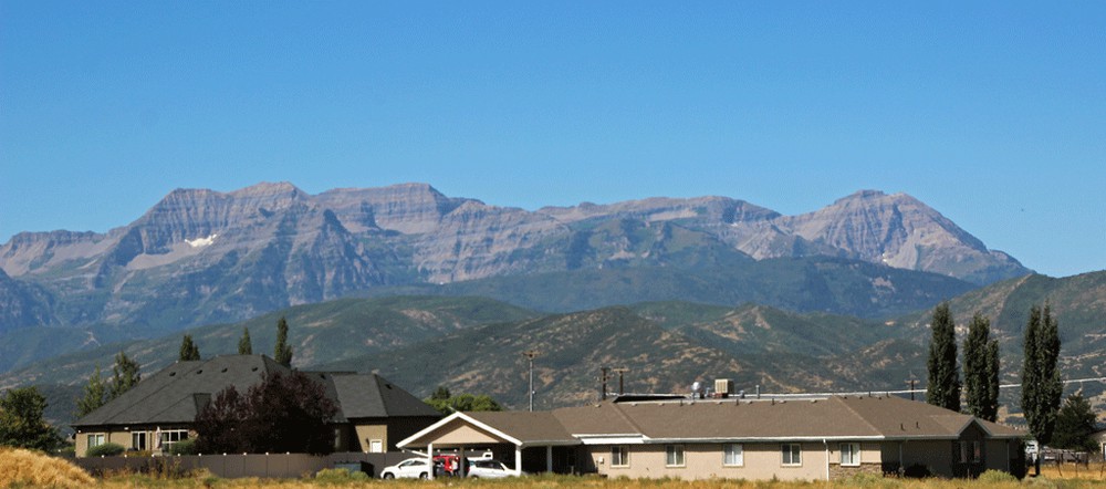 A suburban area with houses in the foreground and a range of mountains in the background under a clear blue sky.