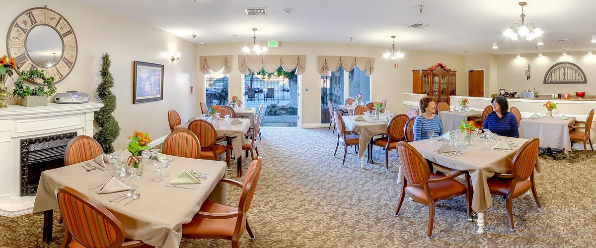 A well-lit dining area with neatly arranged tables and chairs, featuring large windows and elegant decor.