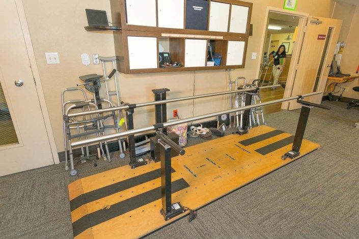 A rehabilitation clinic room featuring parallel bars and various medical equipment for physical therapy.