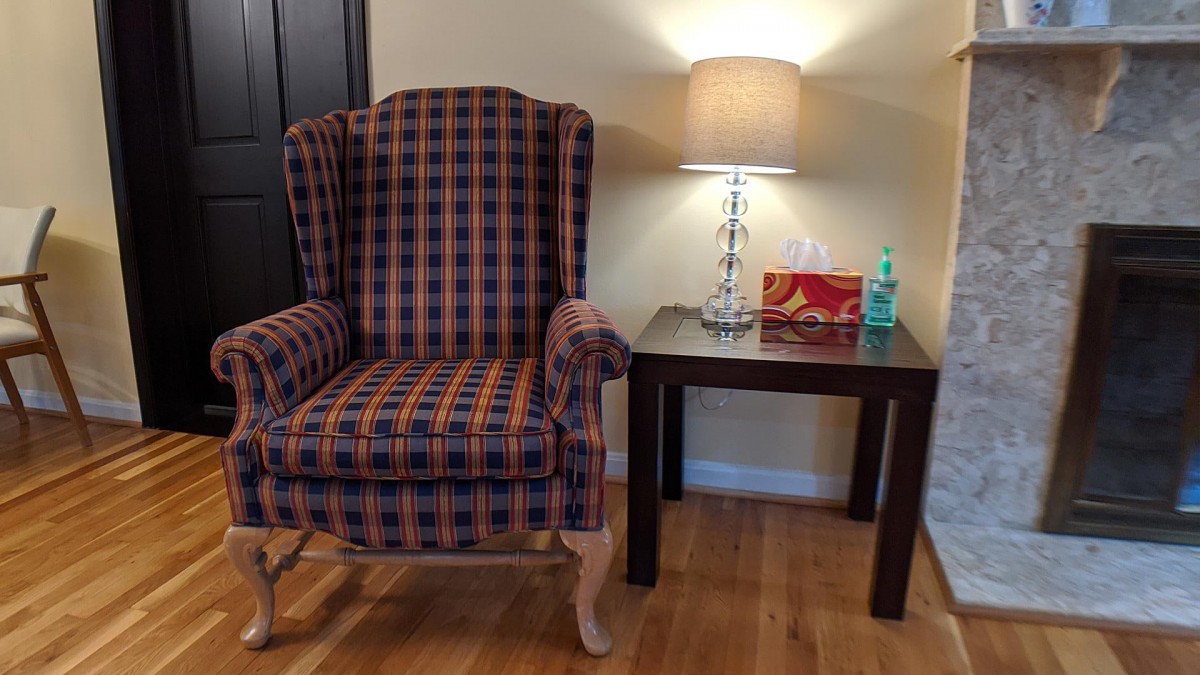 A cozy corner featuring a plaid armchair and a side table with a lamp.