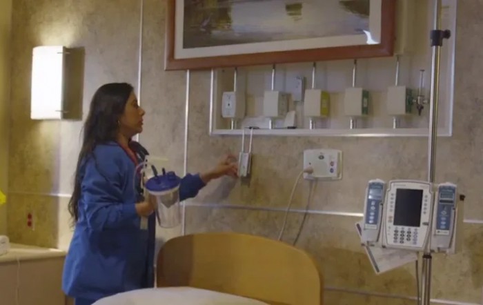 A nurse adjusts equipment in a hospital patient room.