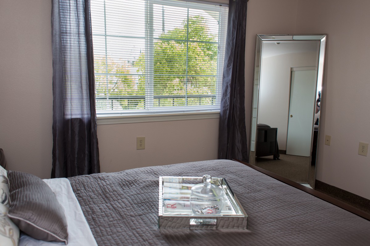 A cozy bedroom with a large window, a mirror, and a neatly made bed featuring a decorative tray.