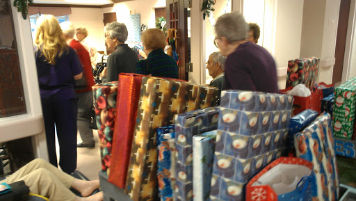 A community gathering with attendees socializing and wrapped gifts in the foreground.