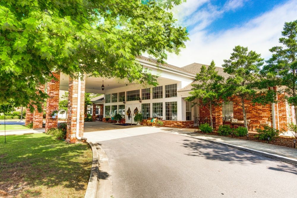 A sunny view of a building entrance with trees and a driveway.