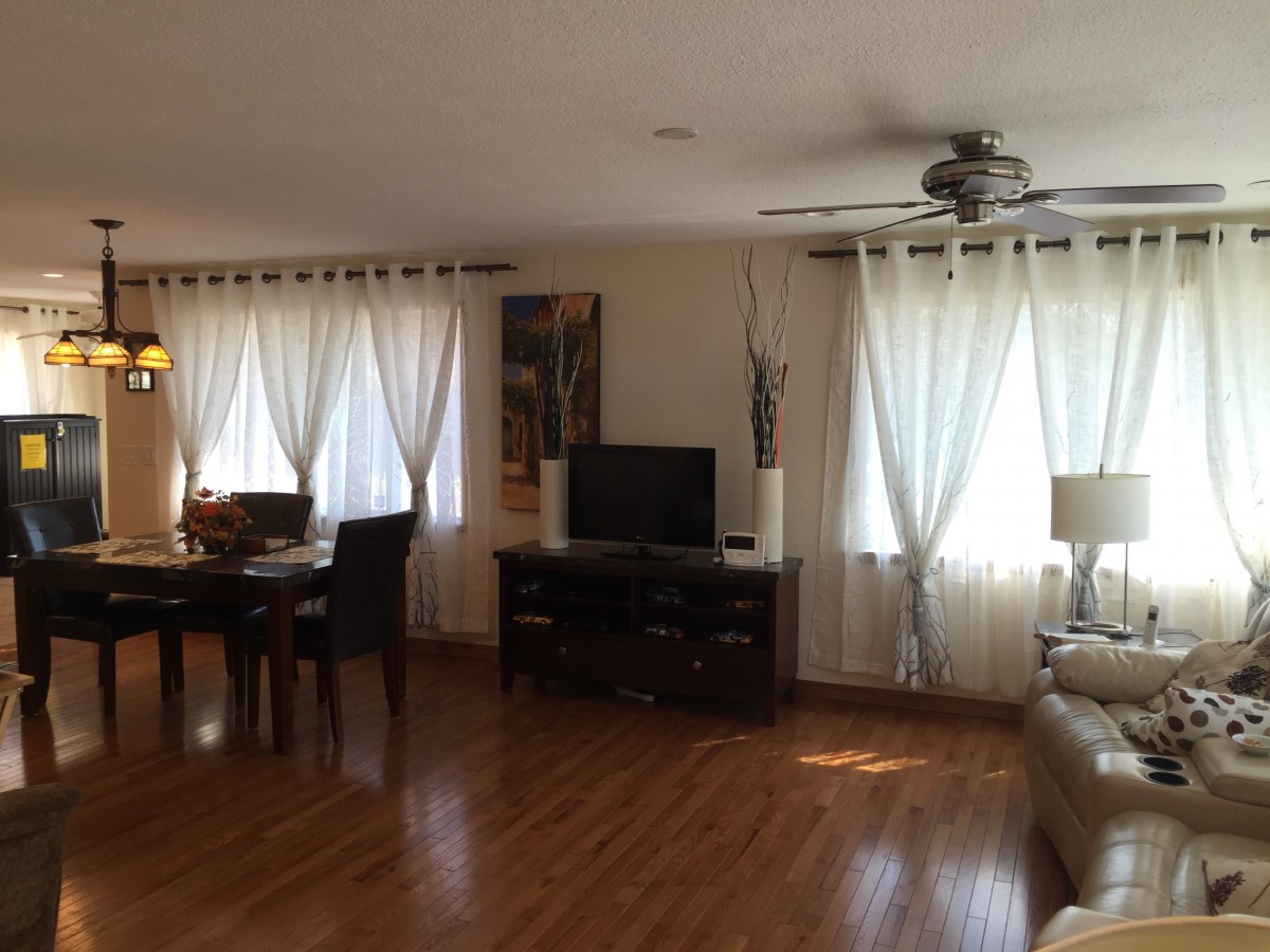 A cozy living and dining area featuring hardwood floors, a television, and ample natural light through the curtains.