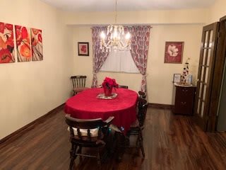 A cozy dining room with a red tablecloth and wooden chairs, featuring a chandelier and decorative artwork.