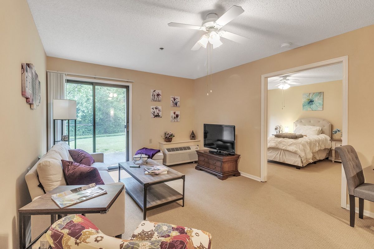 A cozy living room with a sofa, coffee table, television, and a view into an adjacent bedroom.