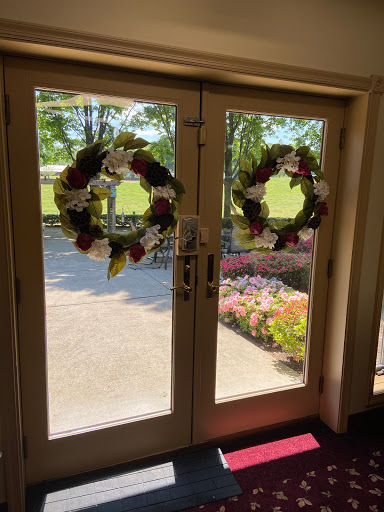 A sunny entrance featuring elegant floral wreaths on double doors, with a glimpse of the beautiful outdoor scenery.