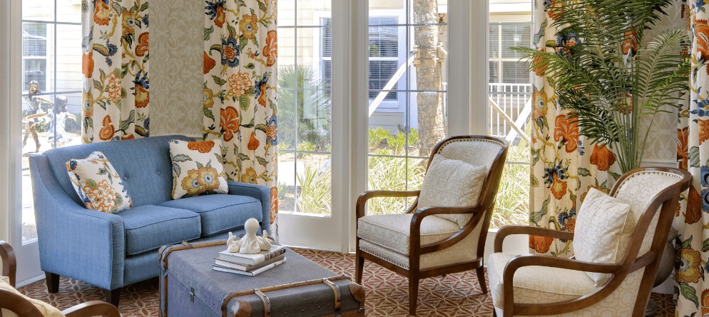 A cozy living room with floral wallpaper and elegant furniture, bathed in natural light.
