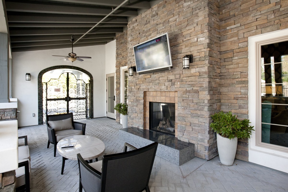 A modern outdoor patio with a stone fireplace and seating area, featuring a wall-mounted TV.