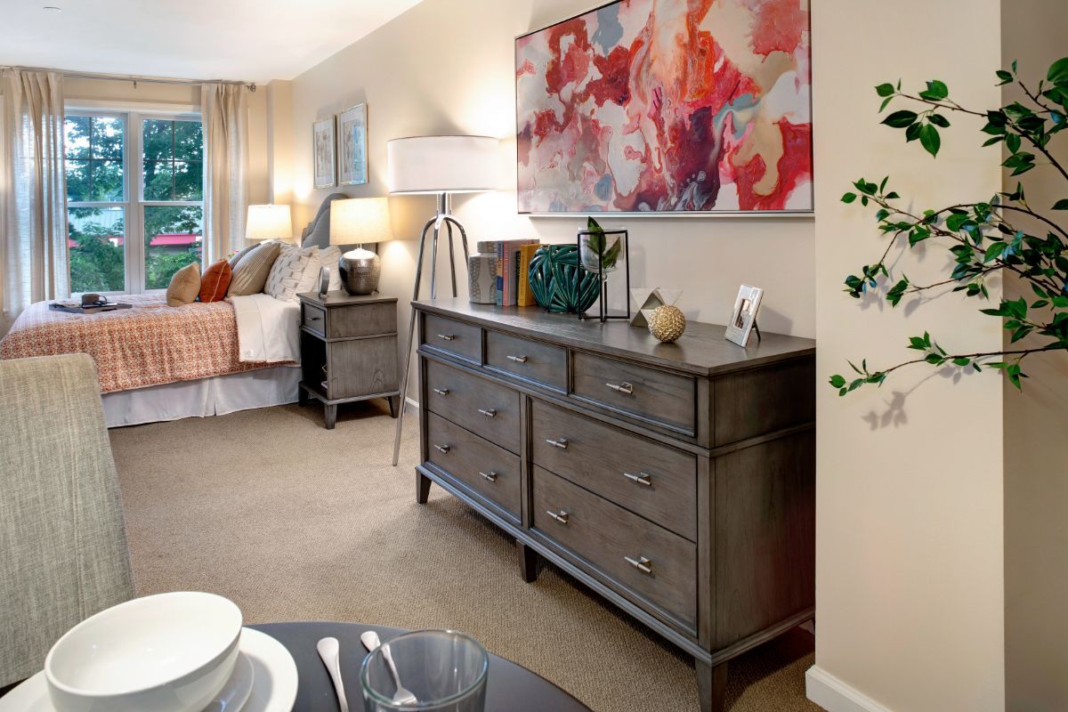 A cozy bedroom with elegant furniture, featuring a dresser adorned with decorative items and a colorful abstract painting on the wall.
