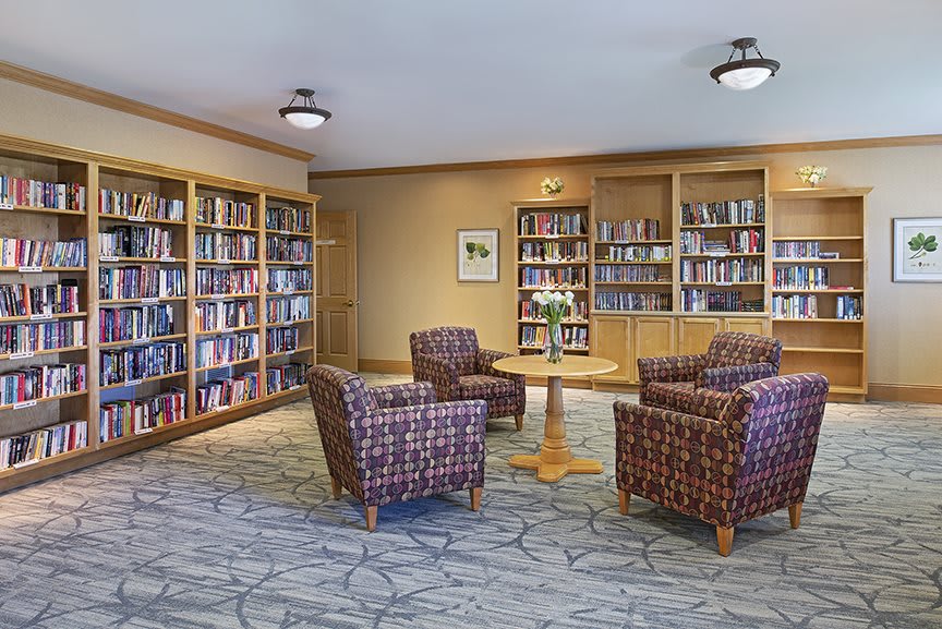 A cozy library corner with bookshelves, comfortable chairs, and a central table for reading.