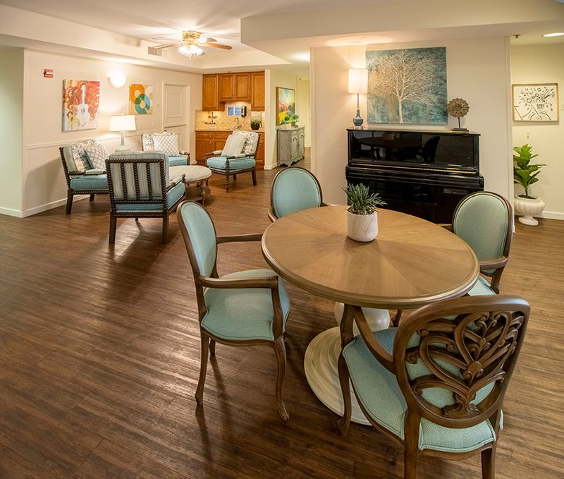 A cozy living area featuring a round dining table, elegant chairs, and a piano, complemented by wooden flooring and tasteful home decor.