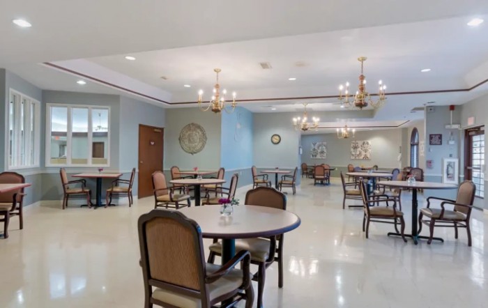 An empty dining room with neatly arranged tables and chairs, illuminated by elegant chandeliers.