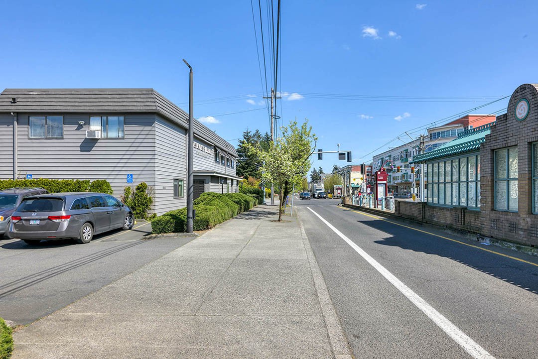 A quiet urban street scene on a sunny day, with sidewalks, buildings, and parked cars.