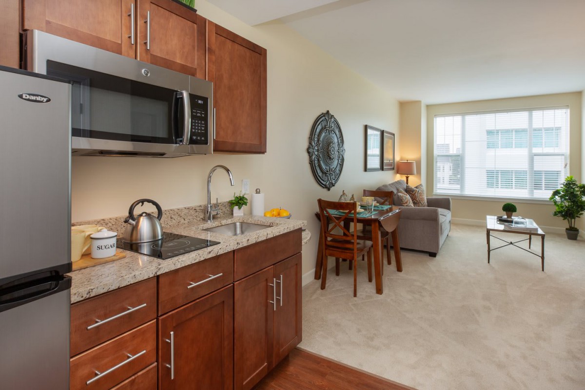 A modern apartment featuring a compact kitchen with wooden cabinets and a cozy living area.