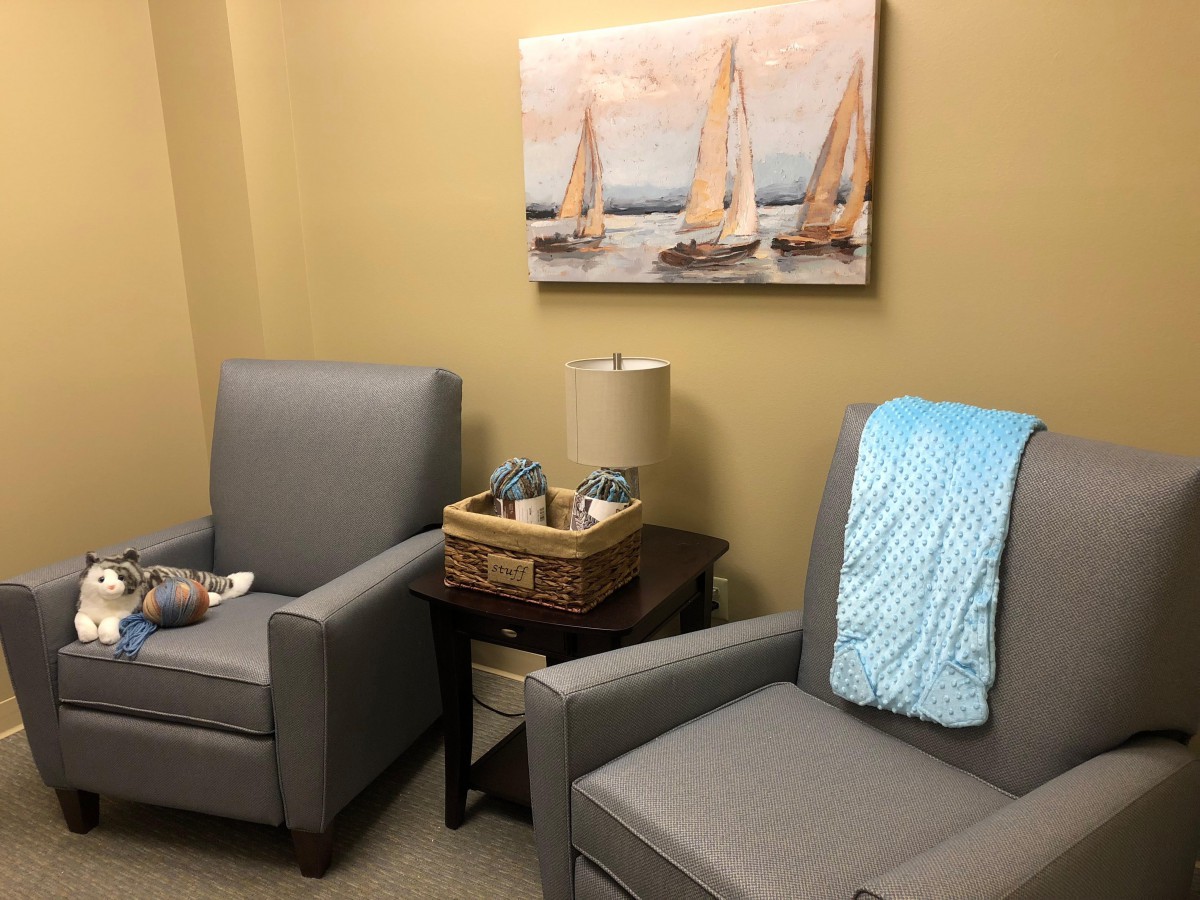 A cozy waiting room with two gray chairs and a seaside painting.