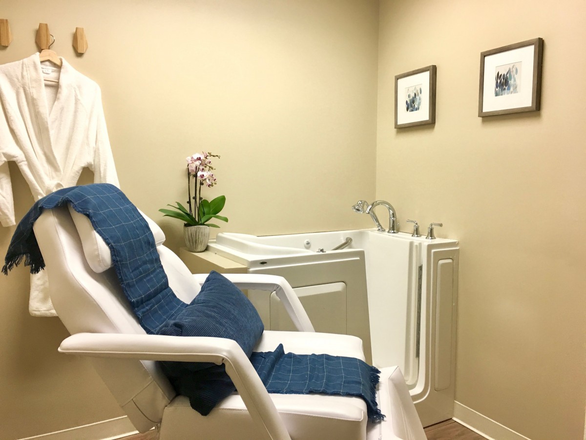 A calming spa room featuring a comfortable chair and a walk-in bathtub with minimalist decor.