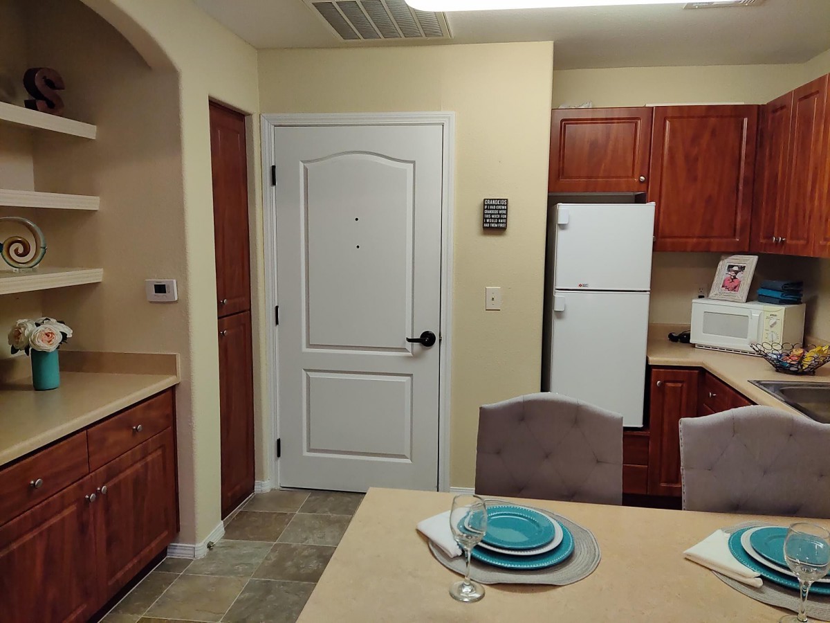A kitchen with wooden cabinets, a refrigerator, and a dining table set with plates.