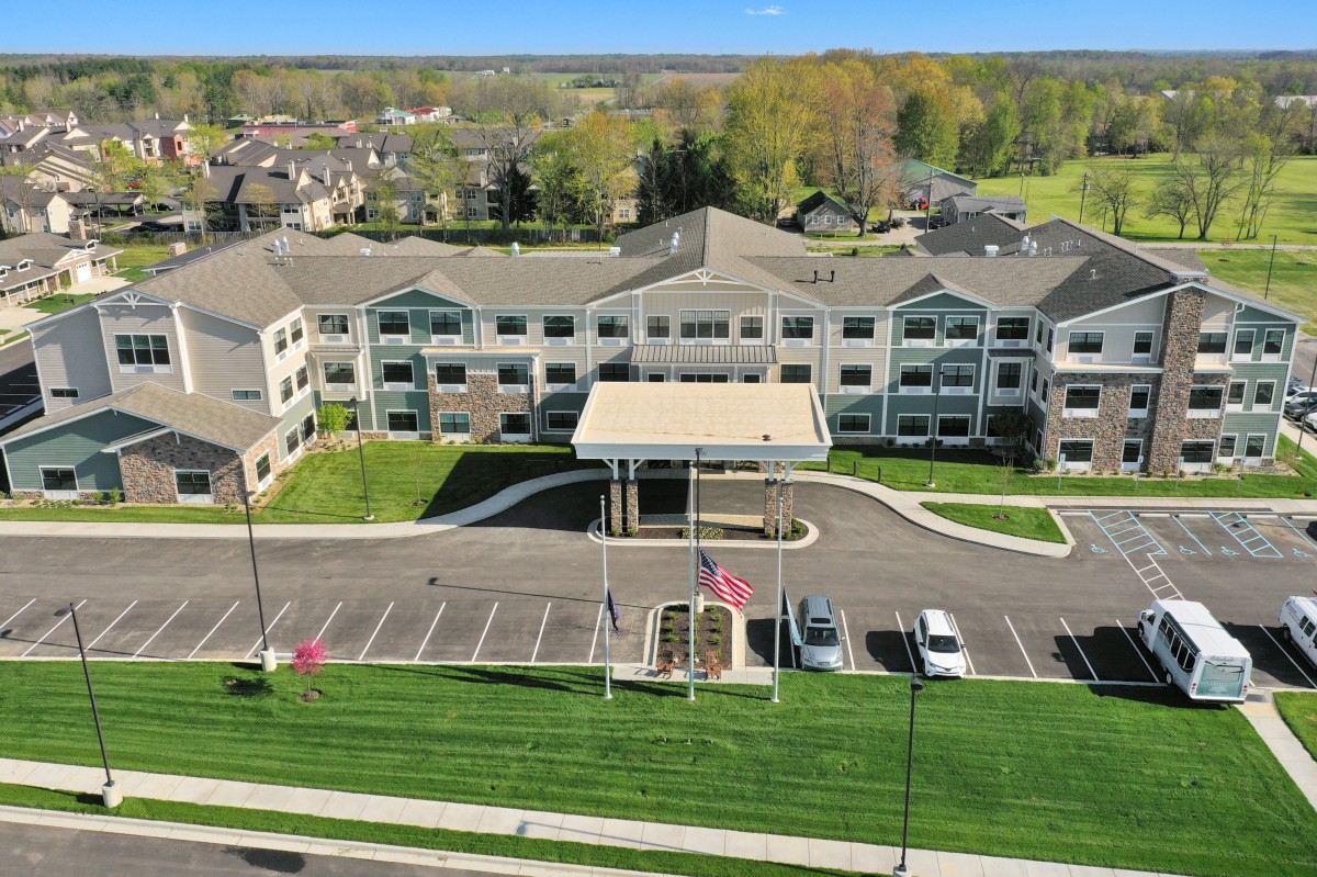 Aerial view of a large residential building with a parking lot and surrounding greenery.