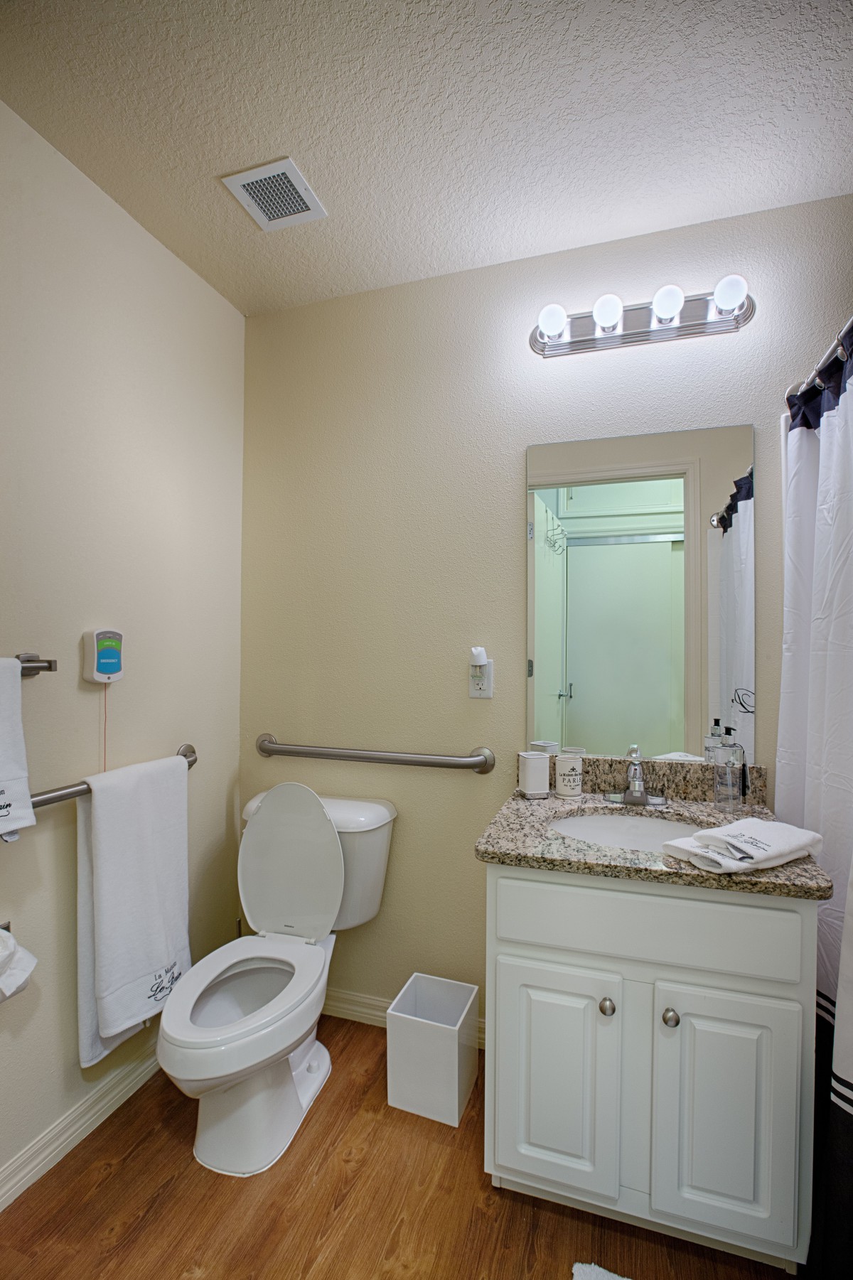 A well-lit bathroom featuring a toilet, sink, mirror, and shower.