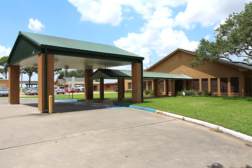 A welcoming entrance to a building surrounded by green grass and a blue sky.