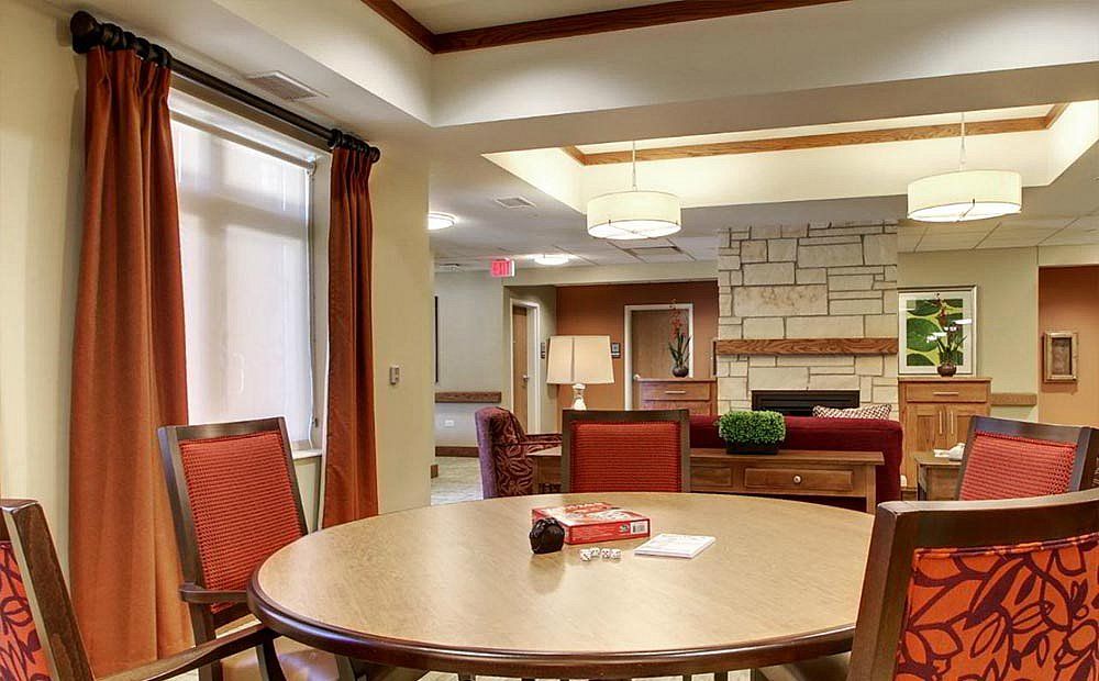 A cozy living room with a central table surrounded by chairs, featuring a stone fireplace and soft lighting.