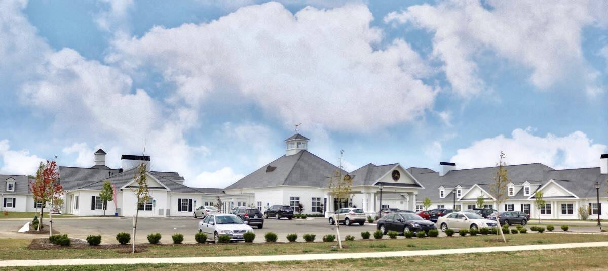 A large building with a parking lot in front, surrounded by cars under a cloudy sky.