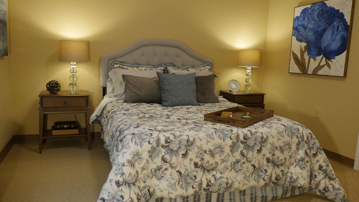 A cozy bedroom with a floral comforter and decorative pillows, flanked by nightstands and lamps.