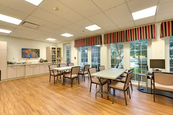A well-lit dining area with tables and chairs, featuring large windows and a wooden floor.