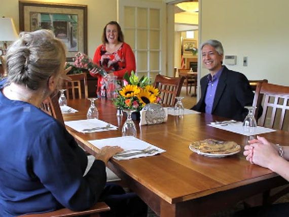 A group of people sitting around a dining table having a discussion with flowers as a centerpiece.