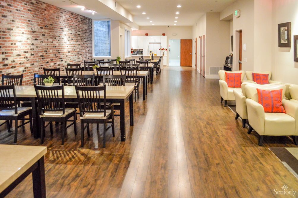 A modern restaurant dining area with wooden floors, tables and chairs, and a brick accent wall.