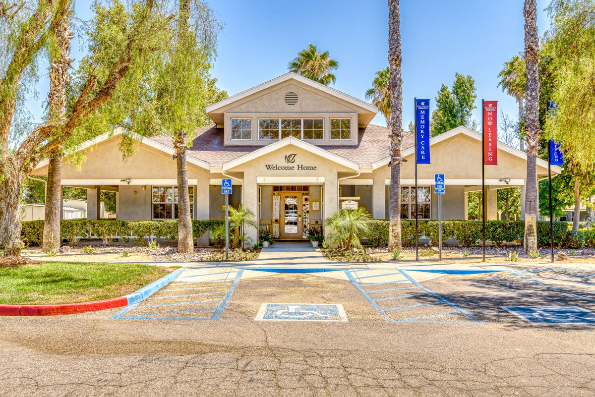 The entrance of a community building with surrounding palm trees and visible parking spaces.