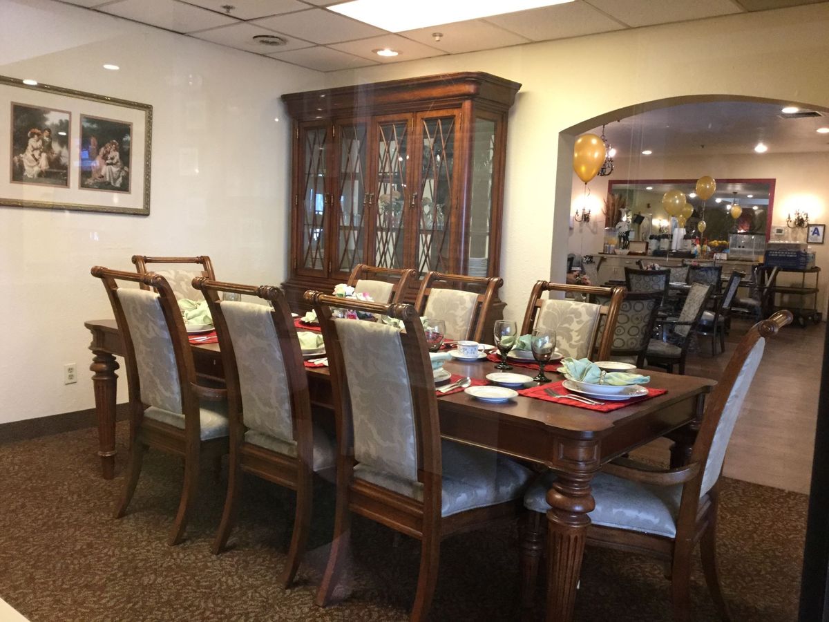 A formal dining room with a large wooden table surrounded by chairs, set for a meal.