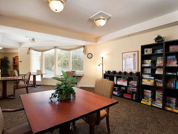A cozy interior space with a dining table, bookshelf, and large windows.