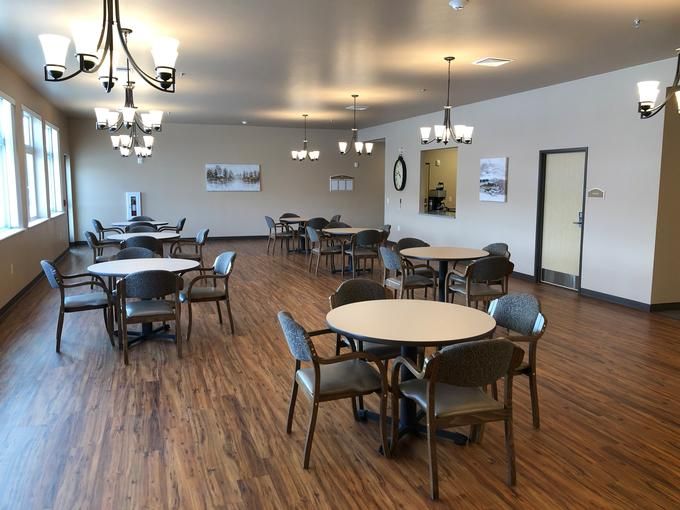 A spacious dining area with round tables and chairs, featuring chandeliers and wood flooring.