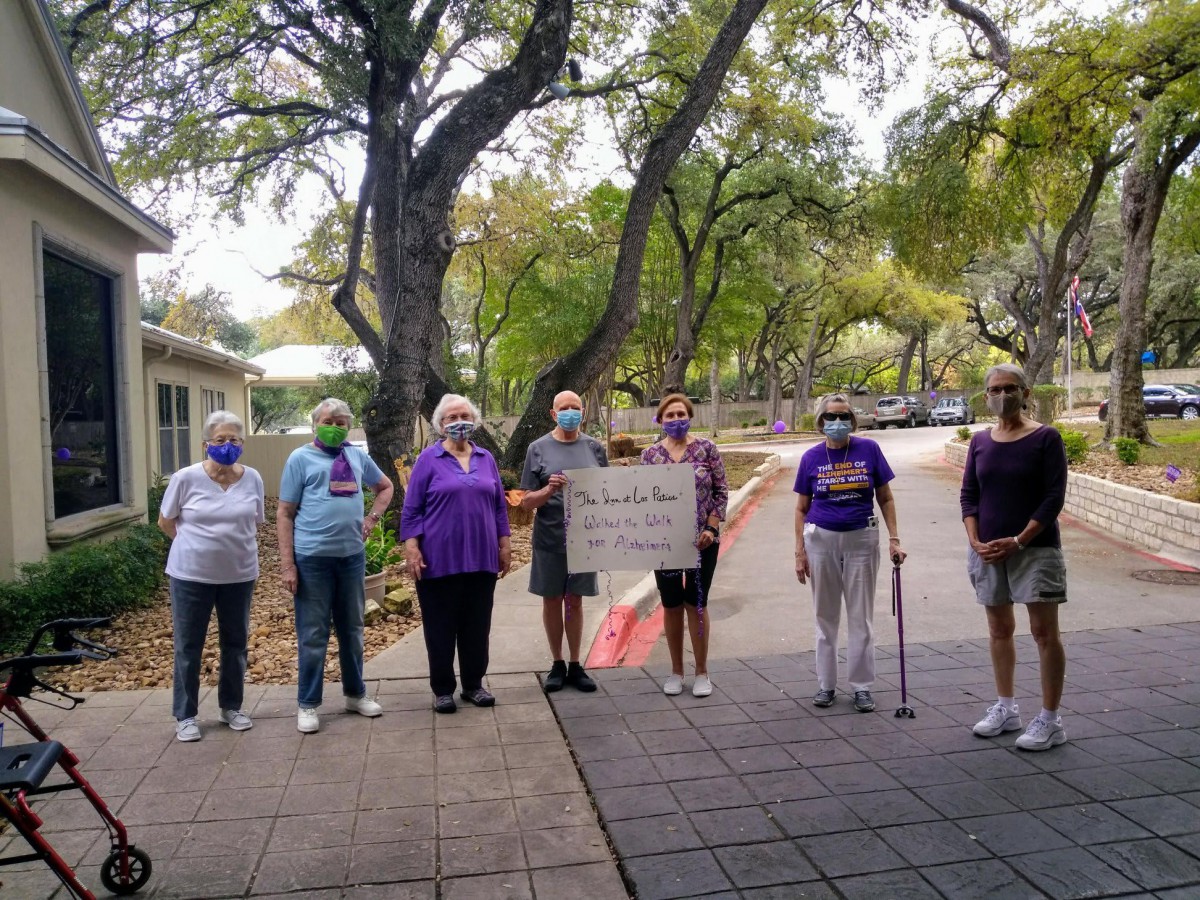 A group of people standing outdoors, one holding a sign, with trees in the background.