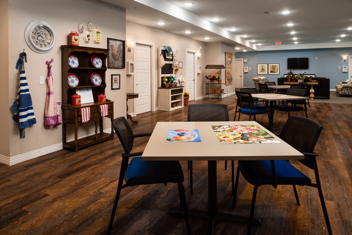 A spacious community room with tables and chairs, featuring art supplies and decorative shelves.