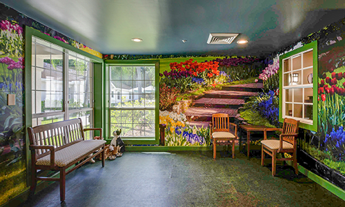 A vibrant indoor space featuring a mural of a garden scene with seating and large windows.