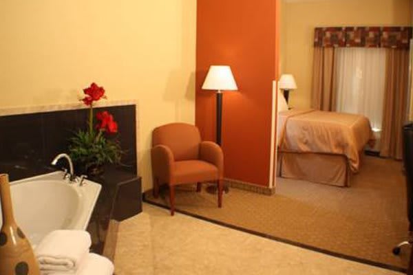 A cozy hotel room with warm tones, featuring a chair, lamp, and bed.