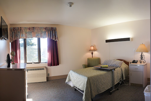 A simple, well-lit hotel room featuring a bed, window, and lamp.